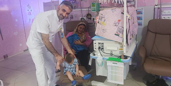 Doctor holds child while mother looks on with baby.